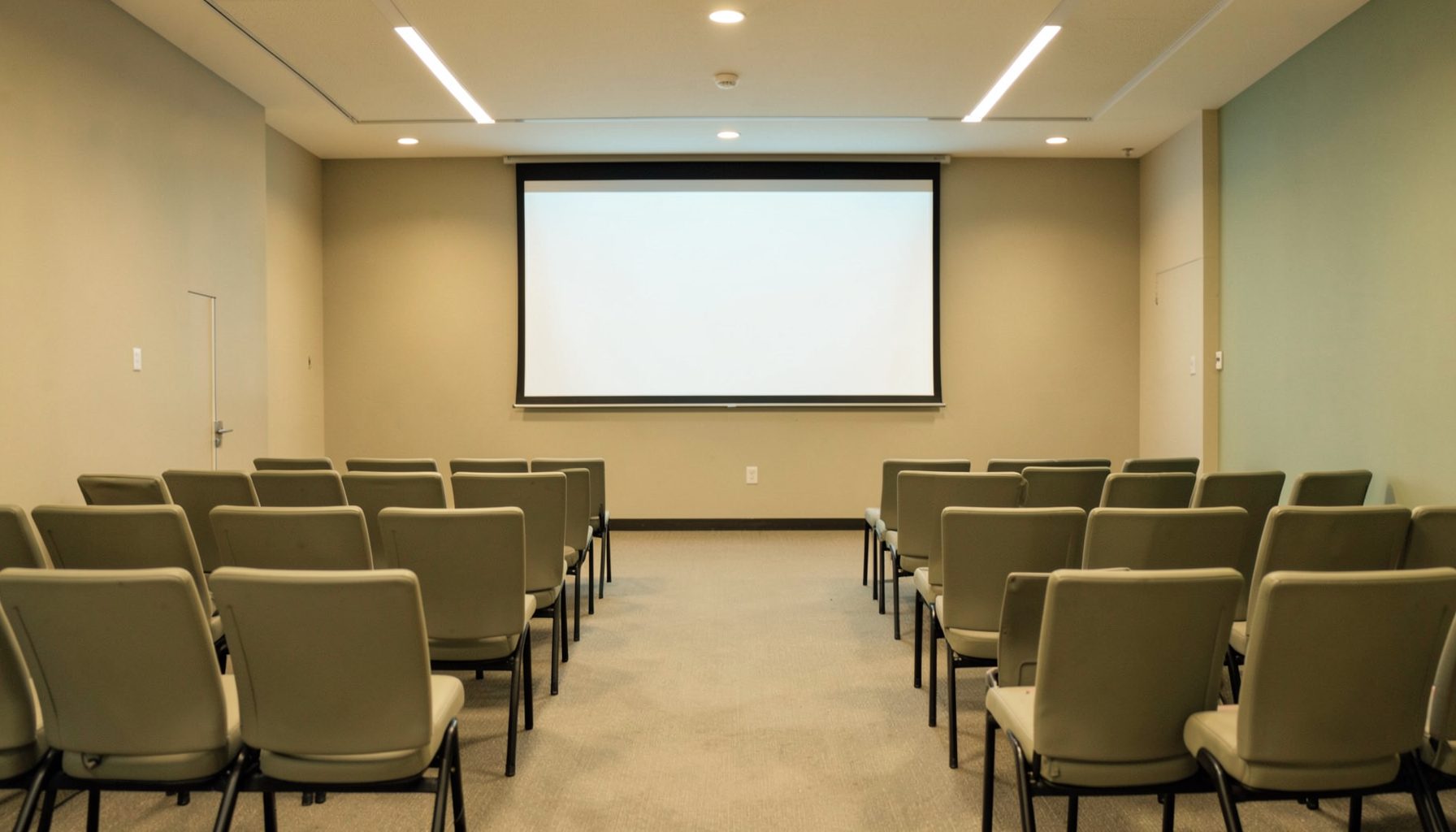 A softly lit seminar room with rows of empty chairs facing a presentation screen, warm beige and sage green tones, calm atmosphere